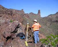 A surveyor using a tripod tool in the middle of a rocky hillside
